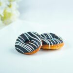 Two chocolate glazed donuts with sprinkles on a white plate, perfect for dessert photography.