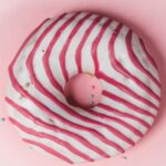 Delicious striped glazed donut on a pastel pink background, perfect for dessert lovers.